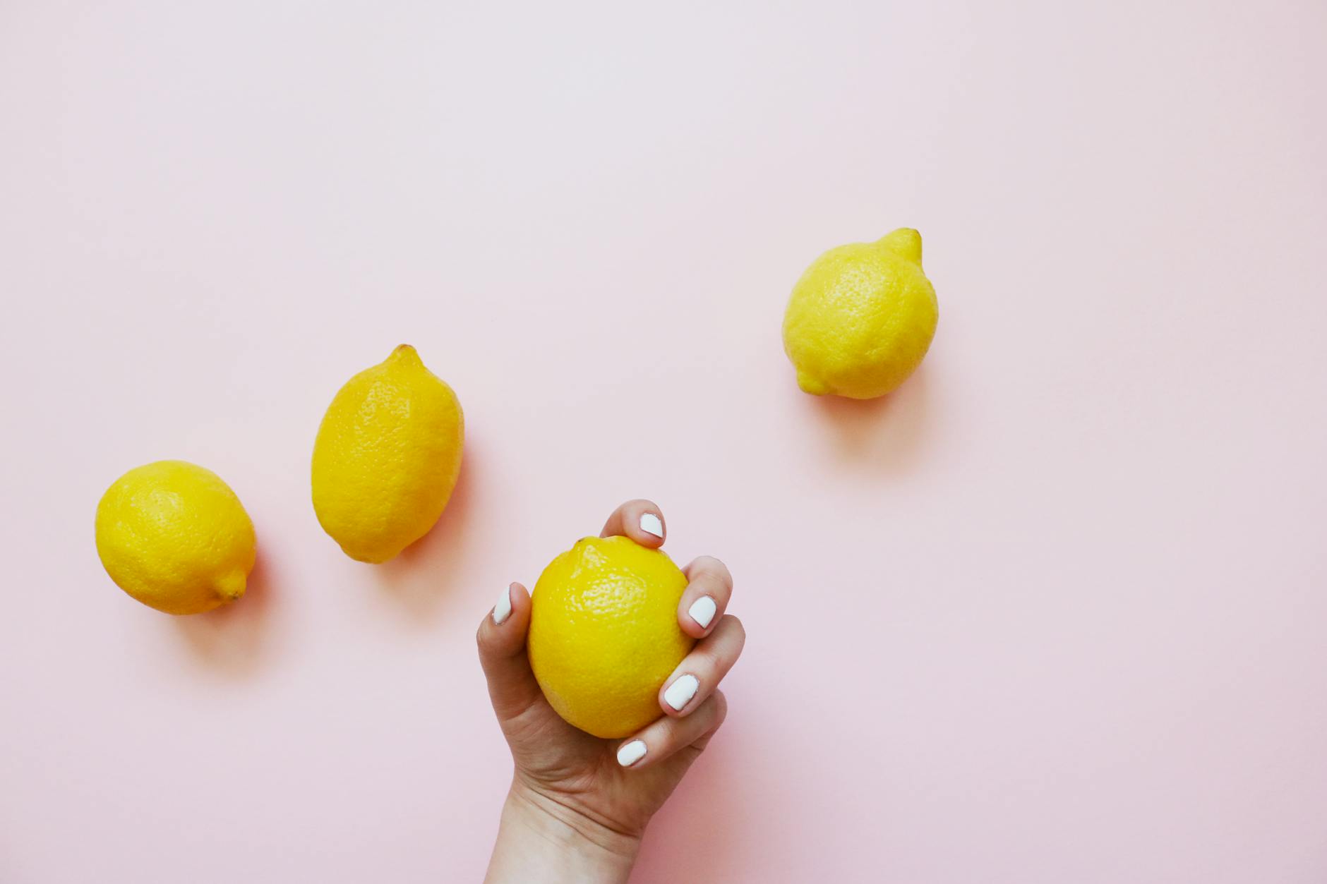 Two hands gently holding lemons together on a soft pink background